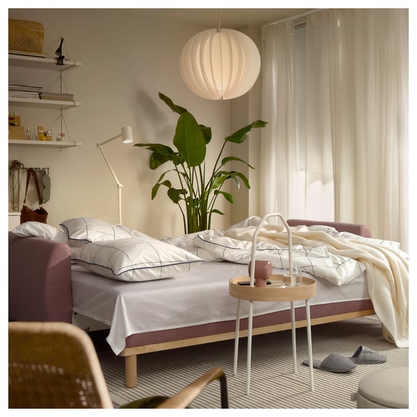 Modern bedroom with white GRUNNARP sofa-bed, purple cushions, plant, wooden side table, and hanging light.