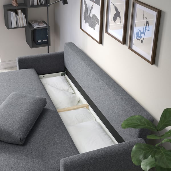 Grey sofa-bed with open storage, pillows, and books.