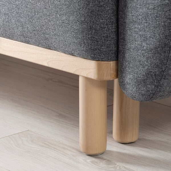 Modern sofa-bed detail: smooth light wood legs, sturdy design, grey comfortable cushions.
