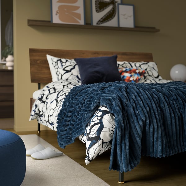 Stylish bedroom with dark blue fleece bedspread, abstract pillows, blue stool, and white slippers.