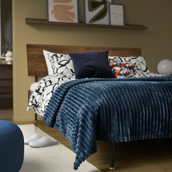 Bedroom with blue bed, pillows, chair, slippers, art.