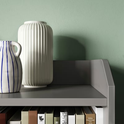 White rippled ceramic vase on grey shelf against green wall.