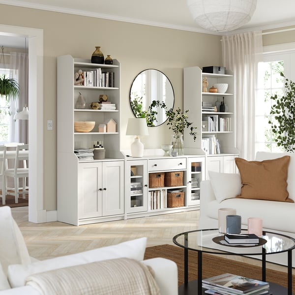 Bright living room with white HAUGA storage units, sofa, and orange pillow. Glass coffee table on rug, with decor and lighting.