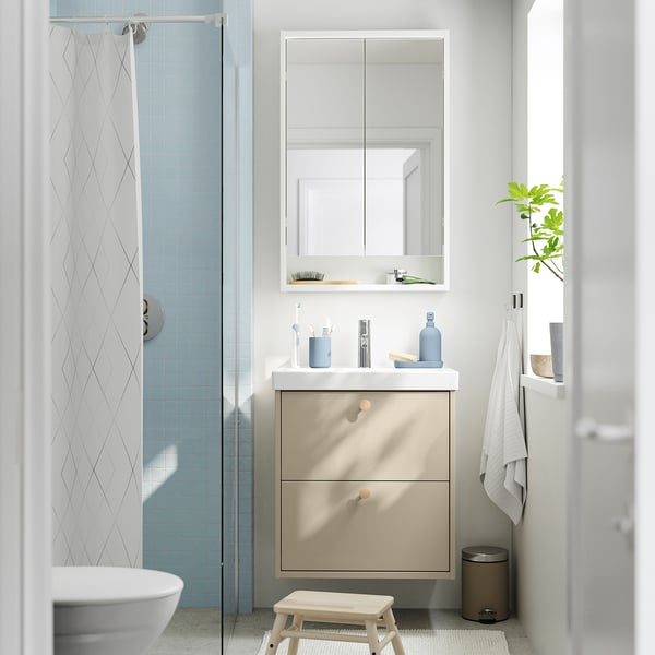 Modern compact bathroom with light beige cabinet, mirror, white sink, and blue-tiled shower.