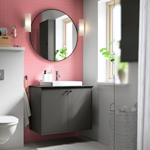 Modern bathroom with dark grey HAVBÄCK cabinet, round mirror, pink tiles, white sink, and wall-mounted toilet.