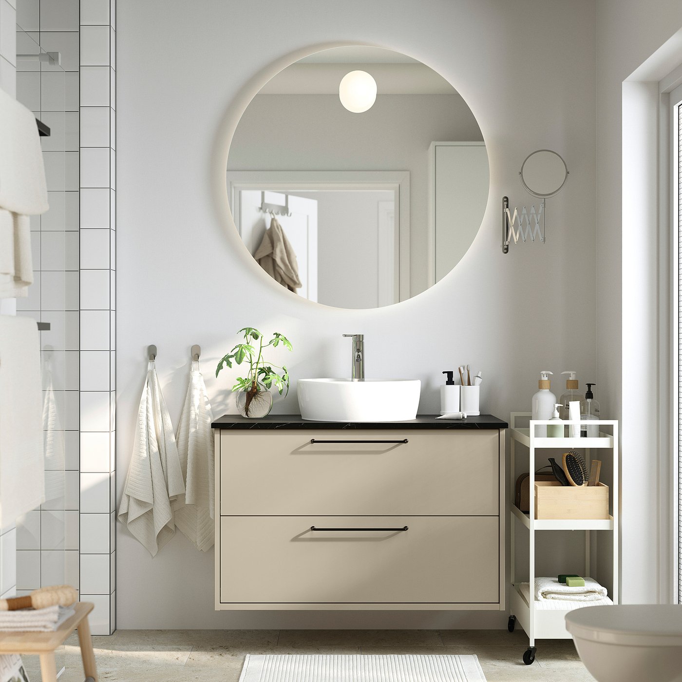 Modern bathroom with hawbäck beige furniture: wall-mounted cabinet, round basin, large mirror, black countertop, small trolley, and plant.