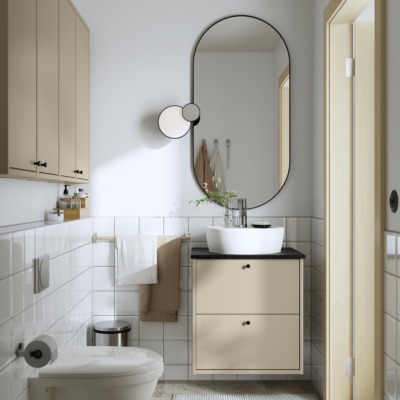 Modern bathroom with beige HAVBÄCK vanity, vessel sink, round mirror, white walls, small plant, two towels, toilet tissue dispenser.