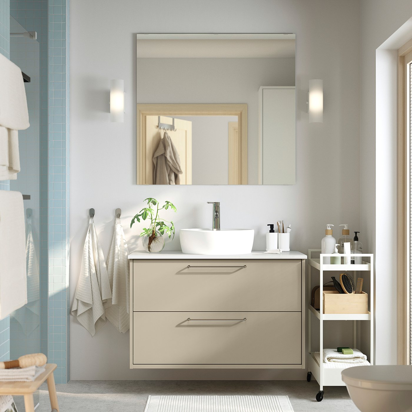 Modern bathroom: beige sink, lights, mirror. Blue tiles, towels, plant.