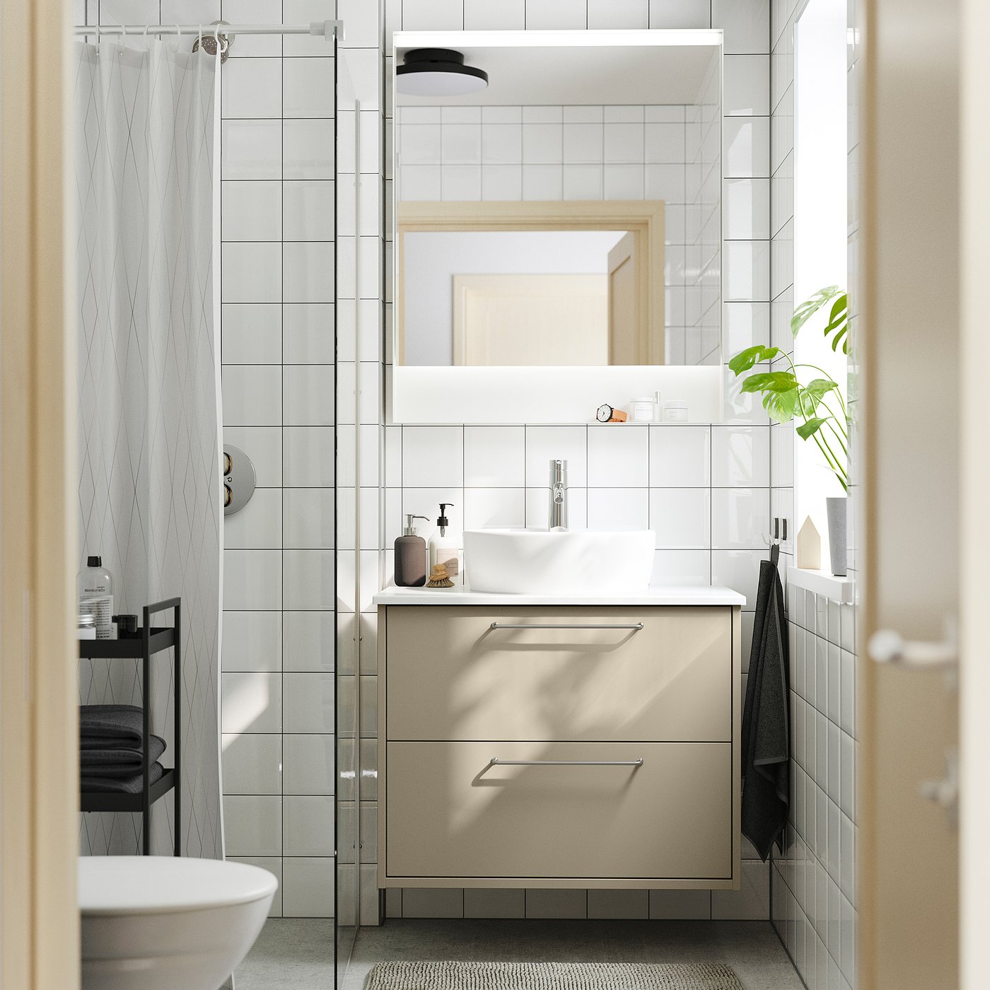 Modern bathroom with beige HAVBÄCK sink, glass shower, mirror, green plant, black towel.