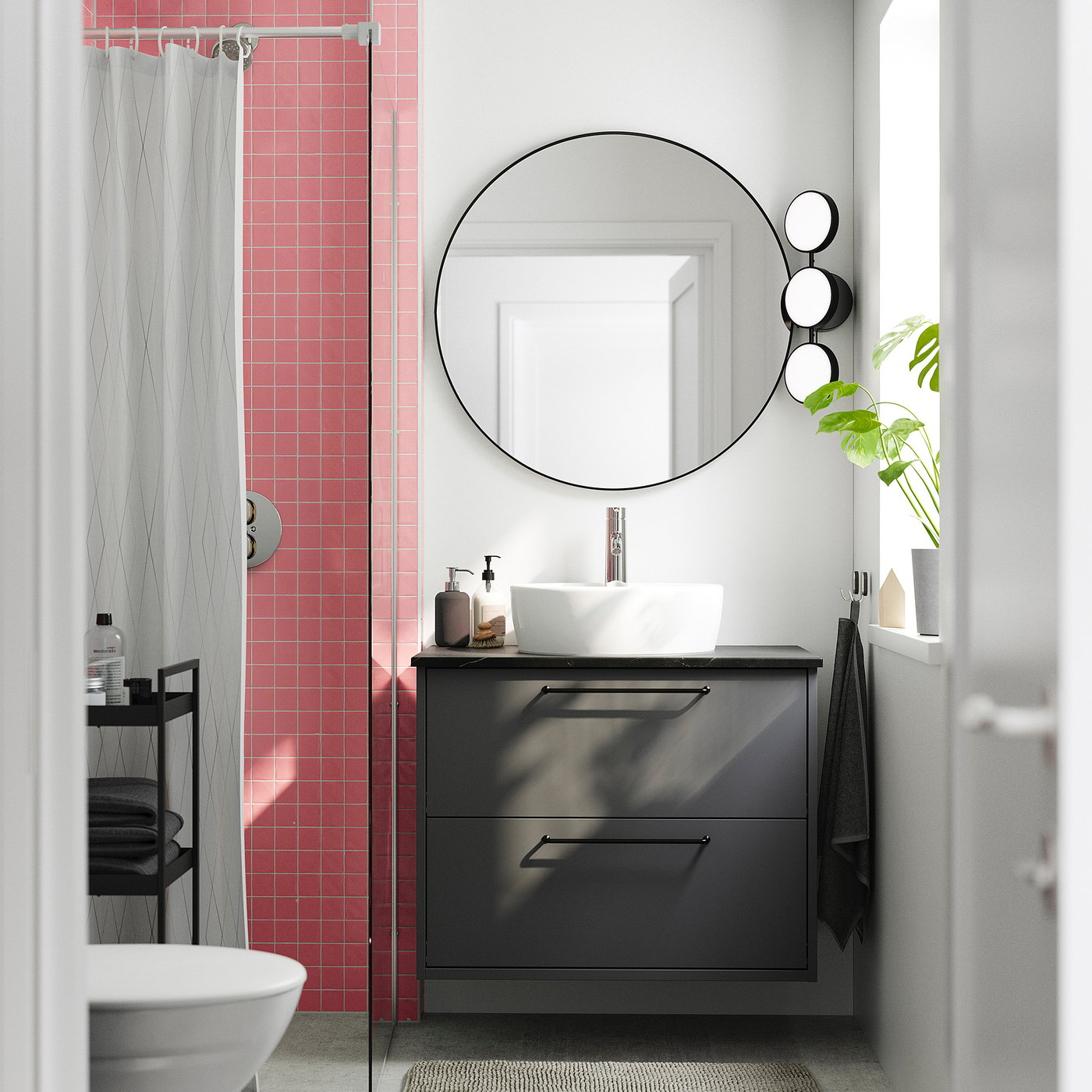 Modern bathroom with HAVBÄCK dark grey cabinet, round mirror, white sink, pink tiles.