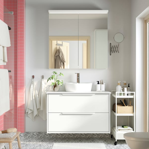 Modern white bathroom with HAVBÄCK vanity, featuring a round basin, mirror cabinet, and storage cart. Clean, minimalist design with black accents.