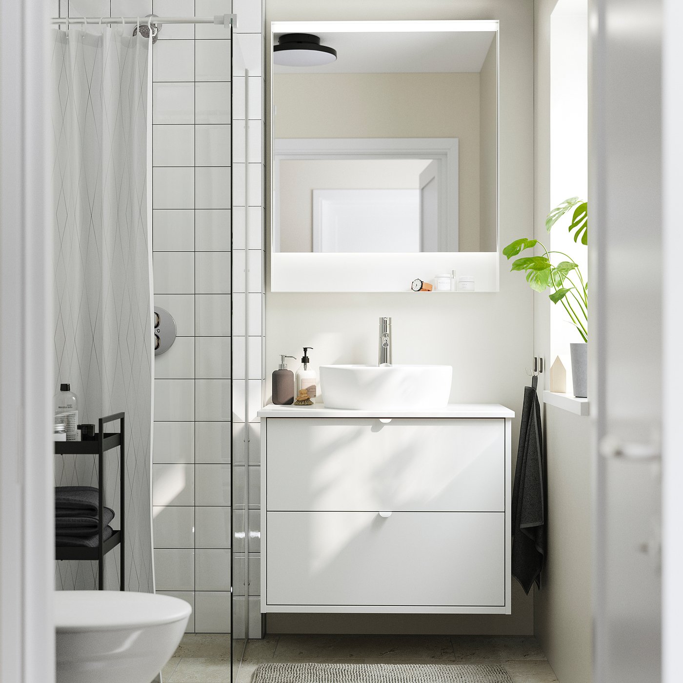 Modern white bathroom: HAVBÄCK unit, rectangular basin, mirror, glass shower, dark towels, and plant on shelf.