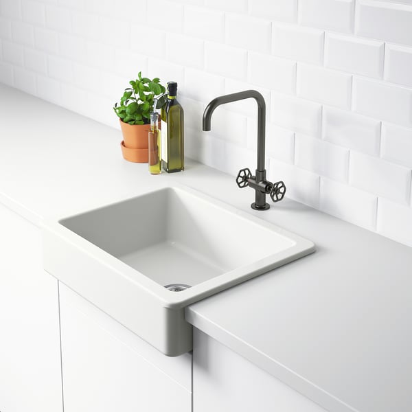 Clean, white kitchen sink with modern, dark tap, set against white tiled wall. The sink an visible front and is part of the HAVSEN series.