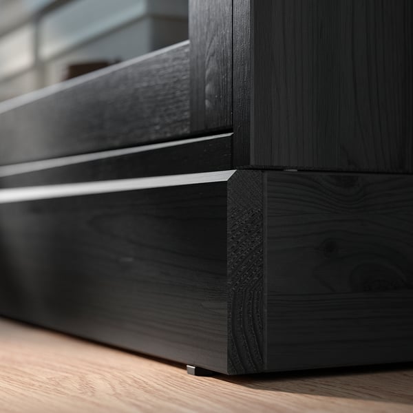 Black wooden furniture corner with sleek lines. Dark finish, smooth surface, and angled joint detail.
