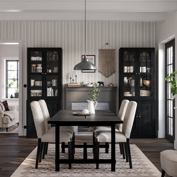 Modern dining room with black HAVSTA cabinets, white dishes, wooden table, neutral chairs, patterned rug, hanging lamp, grey striped walls.