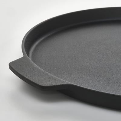 Black cast-iron pizza pan with two handles, displayed on a white surface.