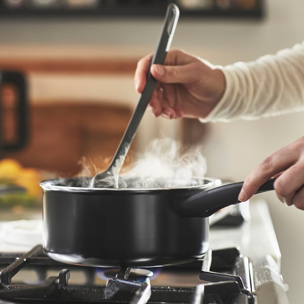 Person cooks on black saucepan with steam, using spoon.