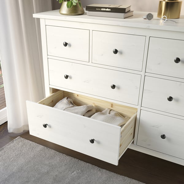Open white dresser with folded clothes, black handles, on rug.
