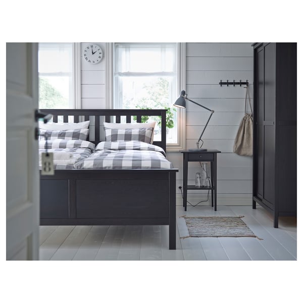 Bedroom scene: black bed with checked sheet, black bedside table with lamp, grey rug, clock on wall.