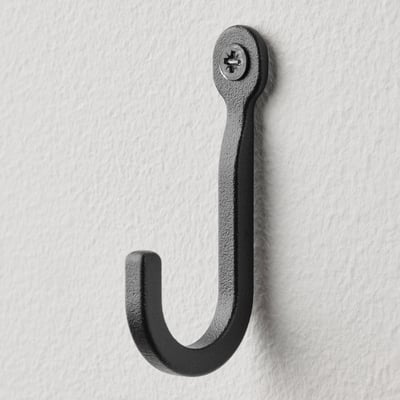 Single black metal hook on white wall, robust and minimalist design.