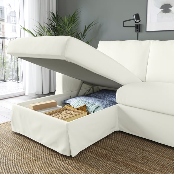 A white sofa with an open storage compartment under the raised seat, revealing blankets and board games.
