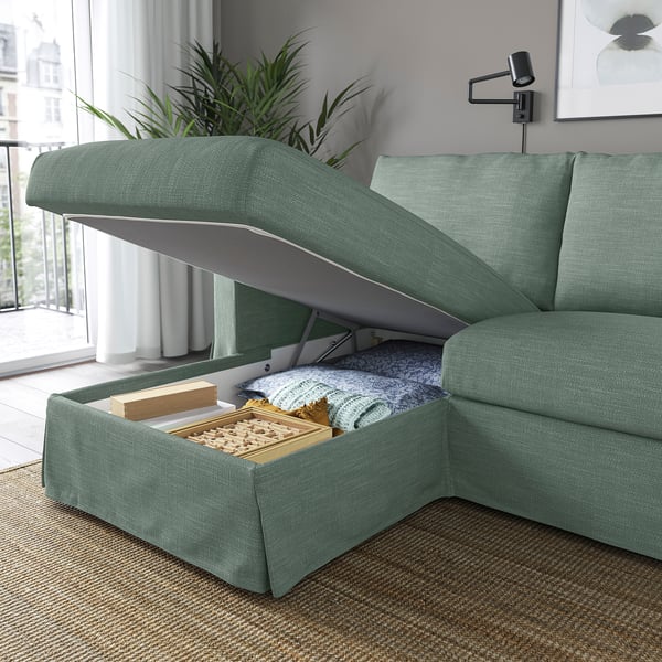 A green fabric sofa with a lifted seat revealing storage space containing blankets and games.