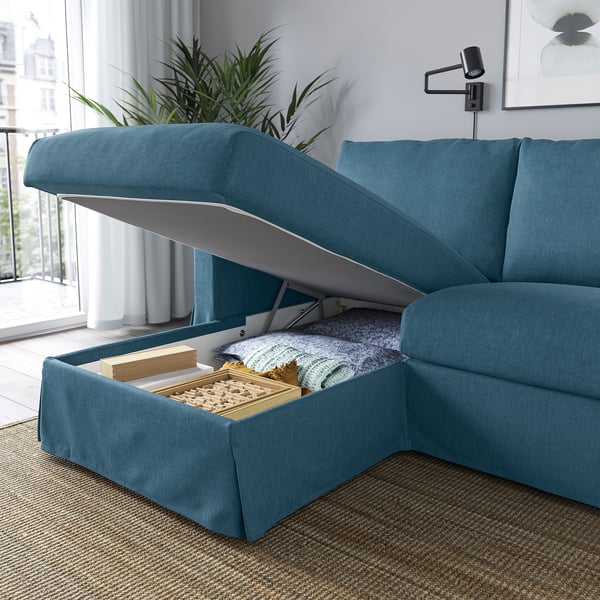 A teal sofa with a storage chaise longue, open to reveal a box of board games and blankets.