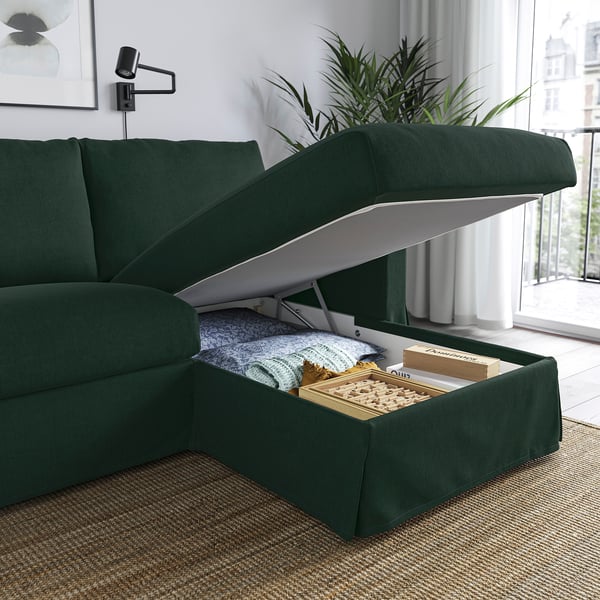 Dark green sofa with open storage compartment showing blankets and a chess set.