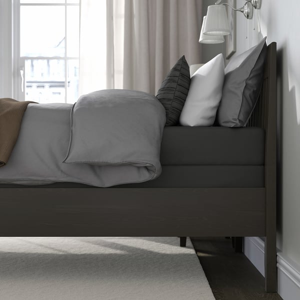 Modern bed with high, dark wooden headboard, grey bedding, pillows, and lamps against a large window. The elevated design offers under-bed storage.