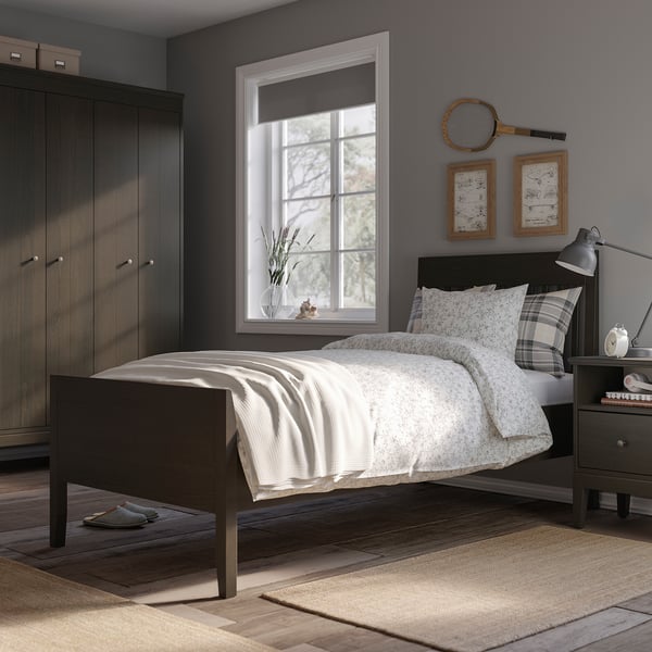 Modern minimalist bedroom an IDANÄS bed with light grey bedding, dark wooden wardrobe, beeswax-colored rug, and decorative tennis racket.