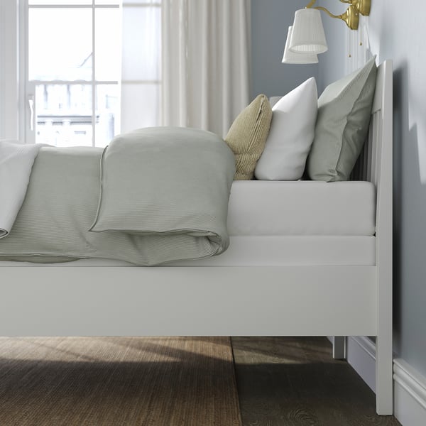 Bed with white mattress, folded grey blanket, and three pillows, featuring sturdy design and under-bed storage.