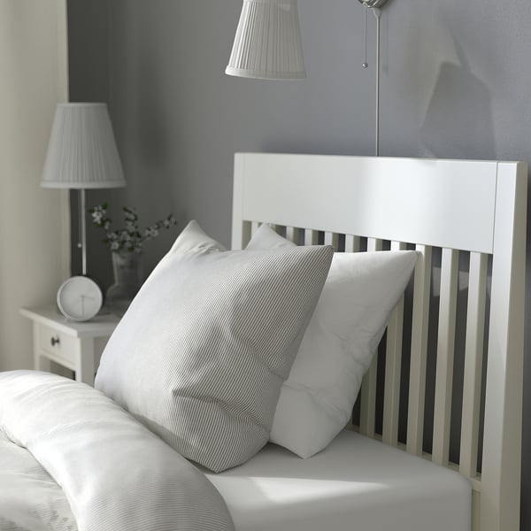 Clean, minimalist bedroom featuring IDANÄS bed with striped pillows, white lamp, and clock, showcasing a tidy, serene atmosphere.
