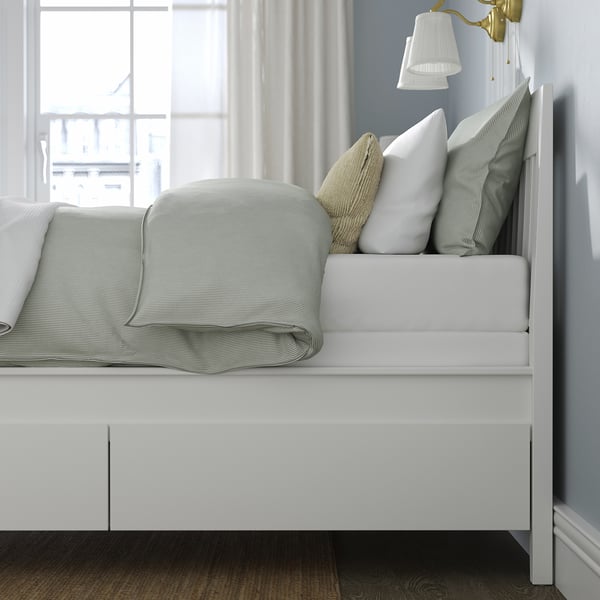 Modern bed with integrated drawers and a mattress base for added height, shown with crisp linens and pillows.