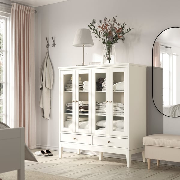 Modern white cabinet with glass doors, towels, lamp, flowers, mirror, window