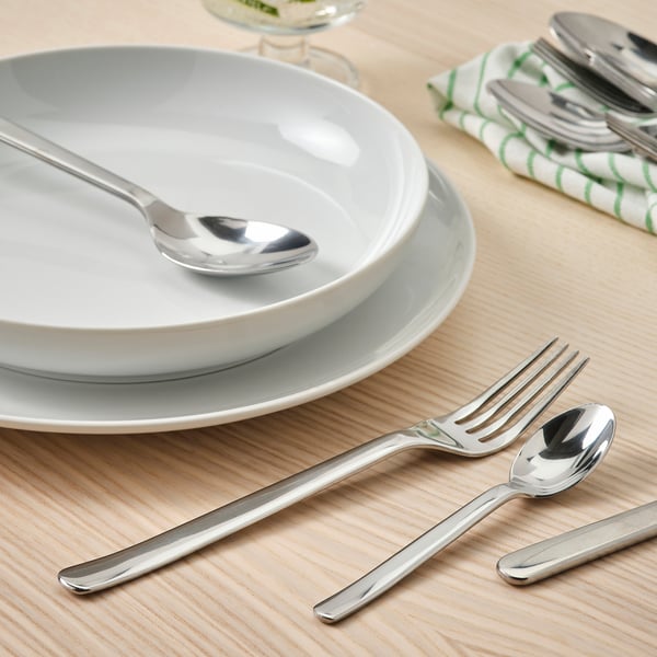 Stacked white plates with silver fork, spoon, and bowl on a wooden table.