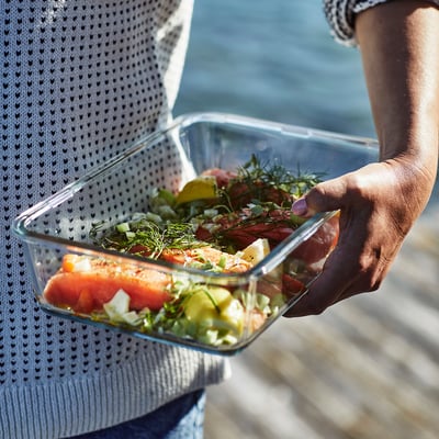 A person holding a glass container with prepared food, likely used for cooking, serving, and storing leftovers.
