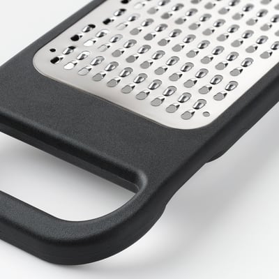 Black kitchen grater with stainless steel surface and plastic handle, designed for efficient and secure use.