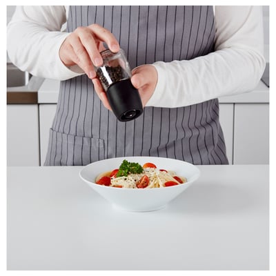 A person grinds pepper into a pasta dish with cherry tomatoes using an IKEA black ceramic spice mill.