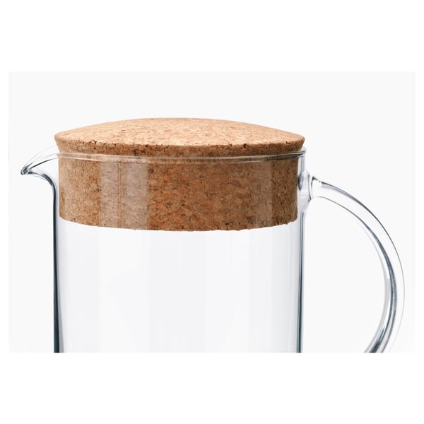 Clear glass pitcher with a sturdy cork lid, designed by IKEA, showcasing quality and simplicity.