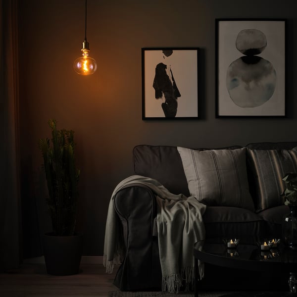 Cosy living space with dark grey couch, grey throw, hanging JÄLLBY light, abstract art, and a potted plant.