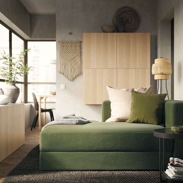 Modern bedroom with green JÄTTEBO sofa, boho wall art, and wooden headboard.