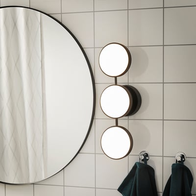 Modern bathroom with round mirror, wall lamp, and dark towels.