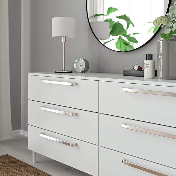 Modern white dresser with sleek metal handles and knobs, a round mirror, and decorative items on top.