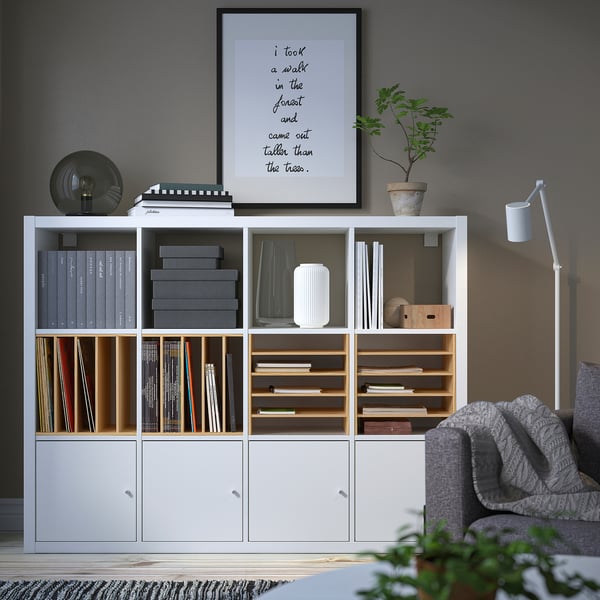 Modern living room with KALLAX shelf, books, decor, grey couch & blanket.