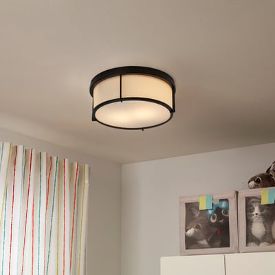 Black KATTARP lamp with frosted glass shade, above colourful curtains, cat photos, and toys on shelf.