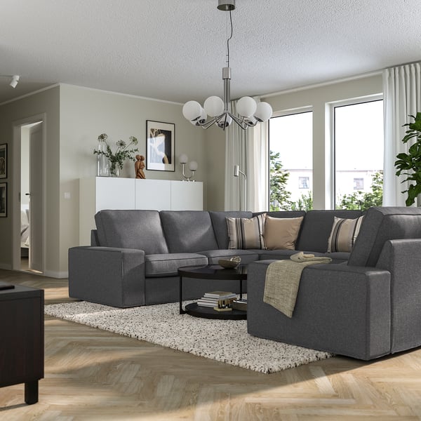 Modern living room with large grey KIVIK sectional sofa and beige pillows, sleek design, and spherical chandelier.
