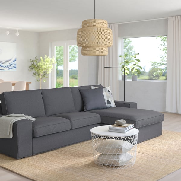 Modern living room with large grey KIVIK sectional sofa, white side table, and natural pendant light. Large windows offer outdoor views.