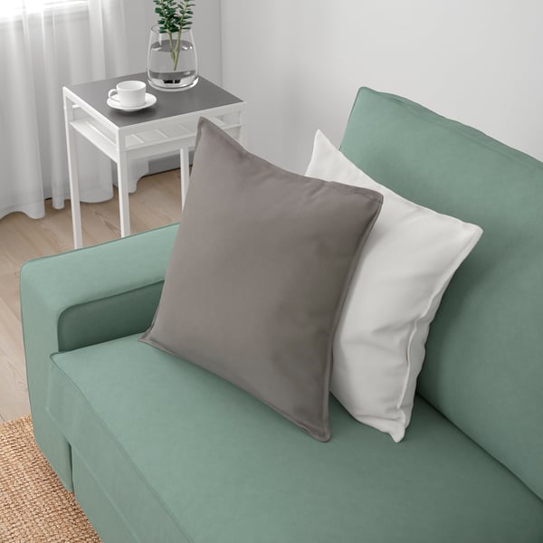 A cosy green sofa with grey and white pillows, ideal for relaxation.