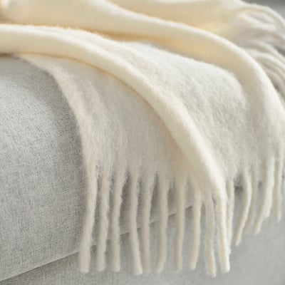 Close-up of a soft, fluffy, off-white throw blanket with fringed edges, draped neatly on a cushion.