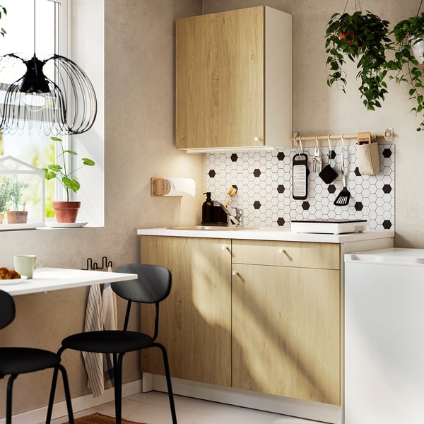Modern compact kitchen with oak cabinets, black tools, and potted plants. Light wood and black accents.